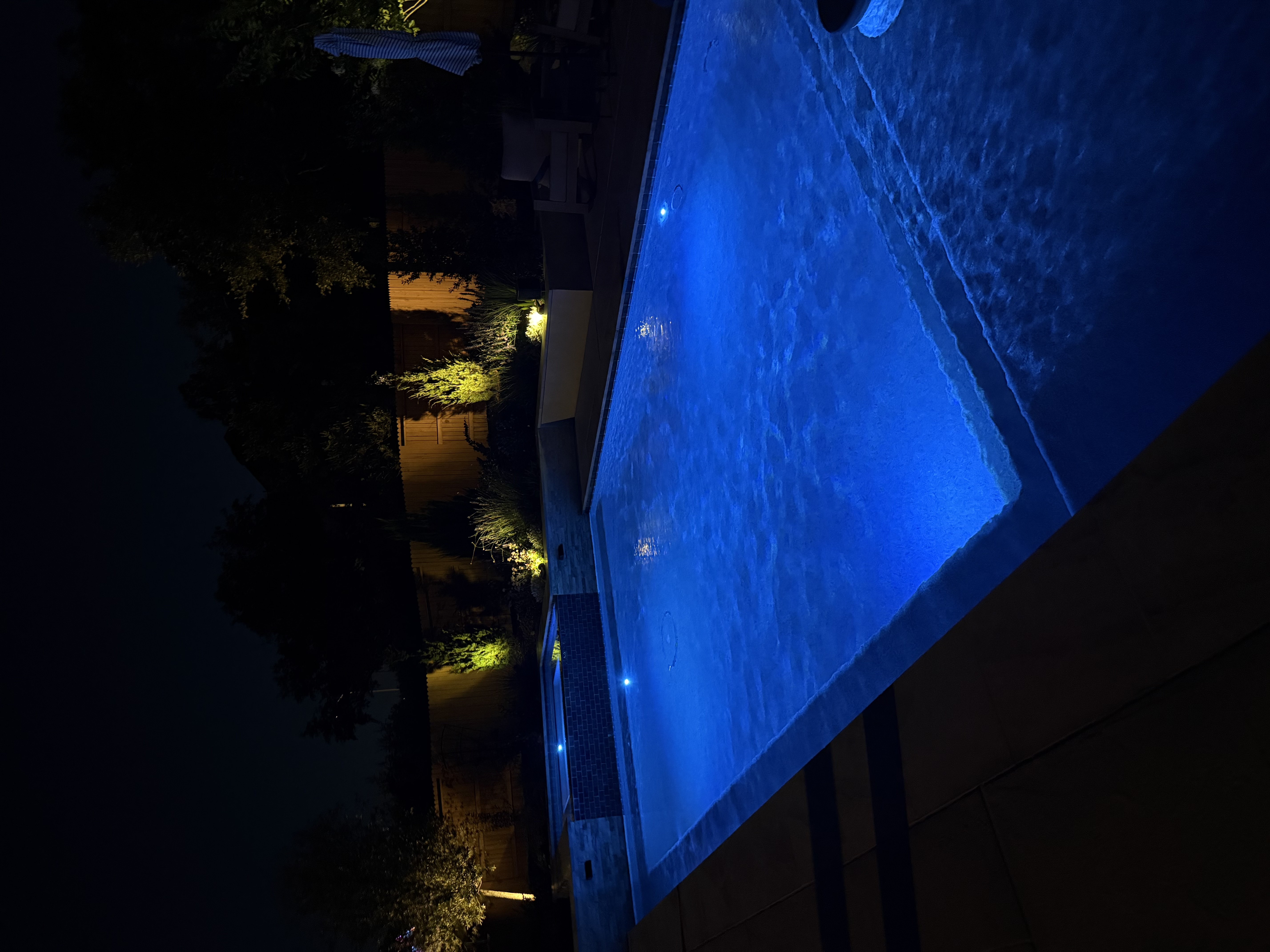 Renovated pool at night glowing blue with new LED lighting and illuminated raised spa and landscaping