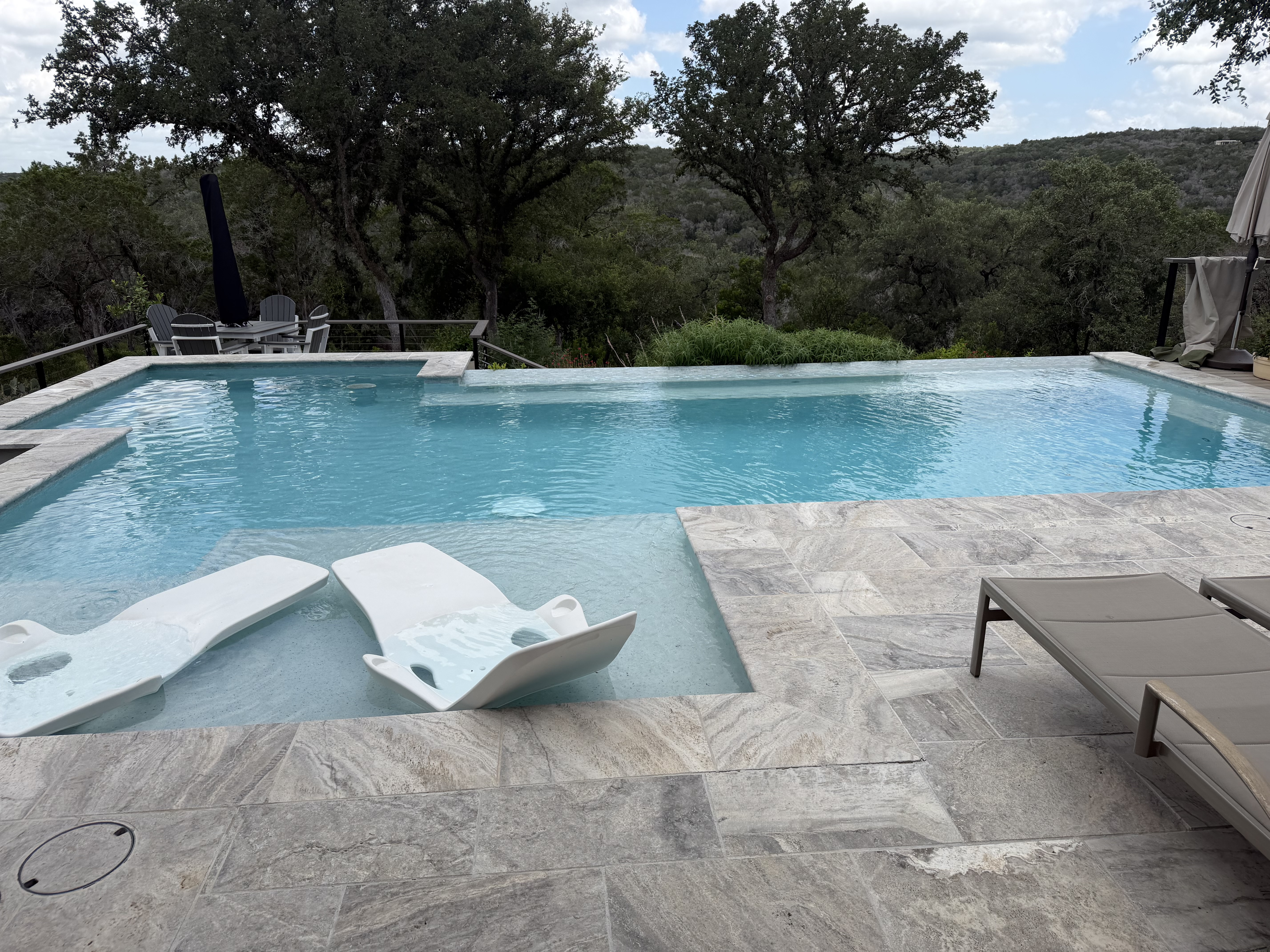 Vanishing-edge custom pool with travertine deck and sweeping Texas Hill Country views under live oaks, built by J. Oliver Pools in Boerne