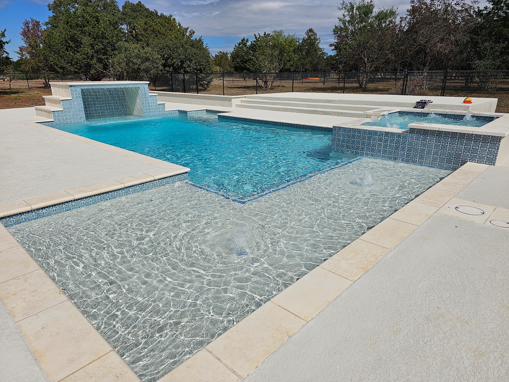 Crystal-blue geometric pool with glass-tile spillway, bubbler tanning ledge, and integrated spa in New Braunfels, Texas